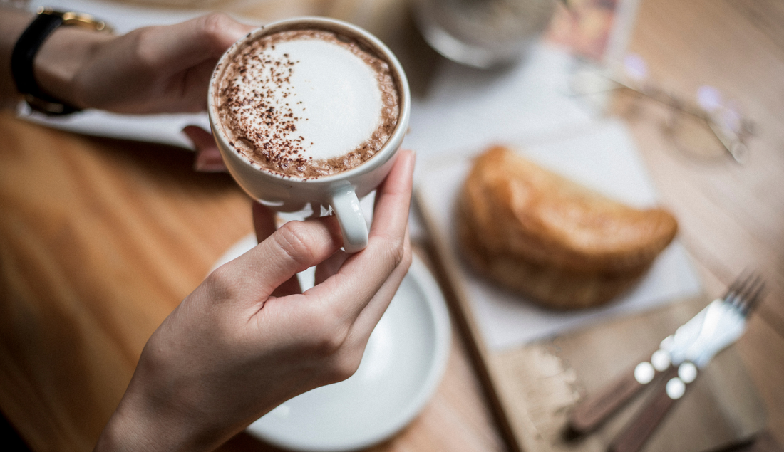 woman in a coffee shop drinking her coffee with a pastry o the table behind