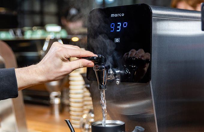 Person using a hot water boiler to pour steamed water into a cup.